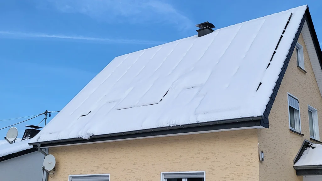 Photovoltaikanlage auf dem Dach eines Hauses, bedeckt mit Schnee, unter blauem Winterhimmel