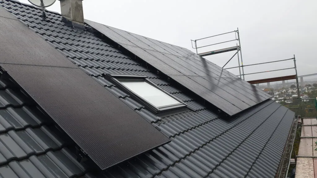 Integrierte schwarze Photovoltaikmodule auf dem Dach eines Wohnhauses in Siegen mit effizienter Batteriespeicherung bei trübem Wetter